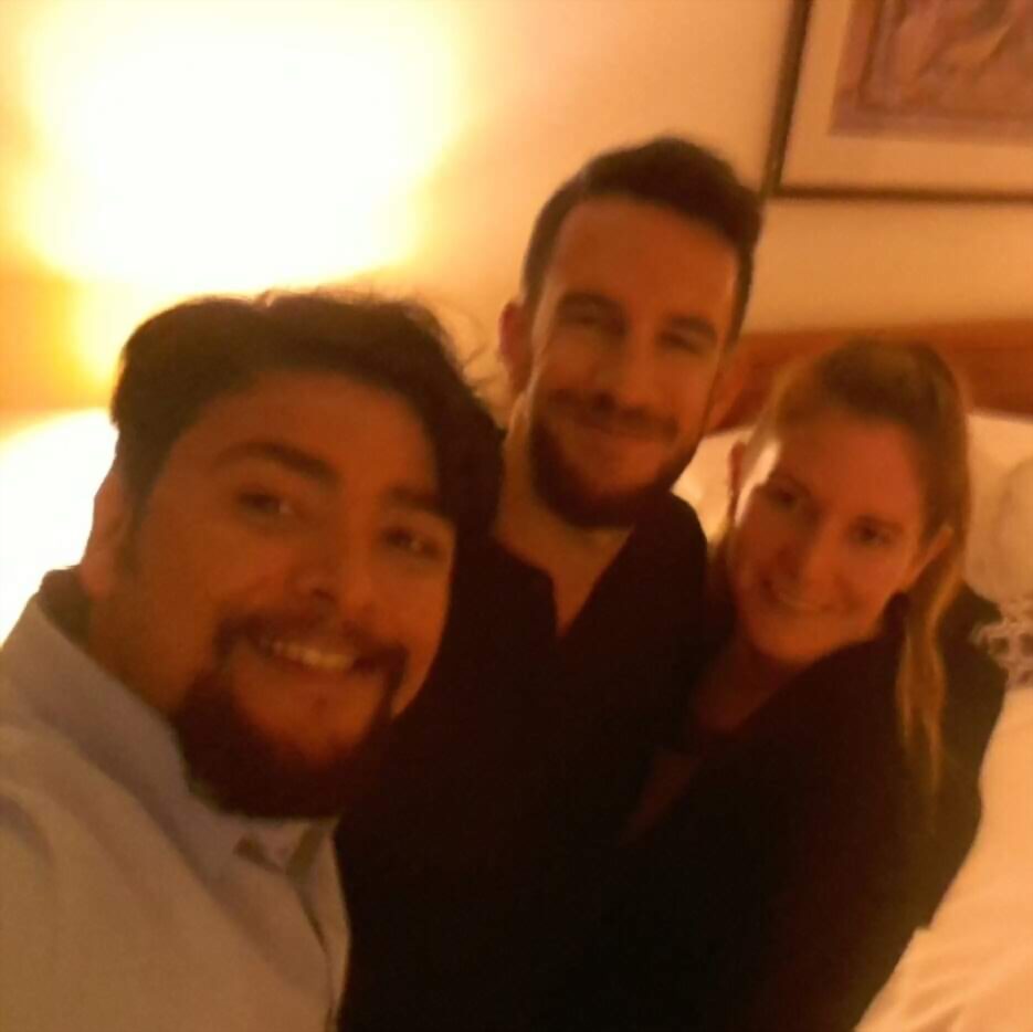 A close, motion-blurred phone selfie of three smiling friends in a room lit by a bedside lamp